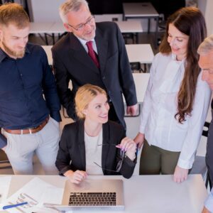 Group of five people discussing around a laptop in an office setting.