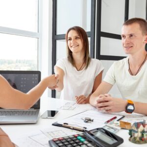Three people discussing documents at a table with a laptop and calculator.