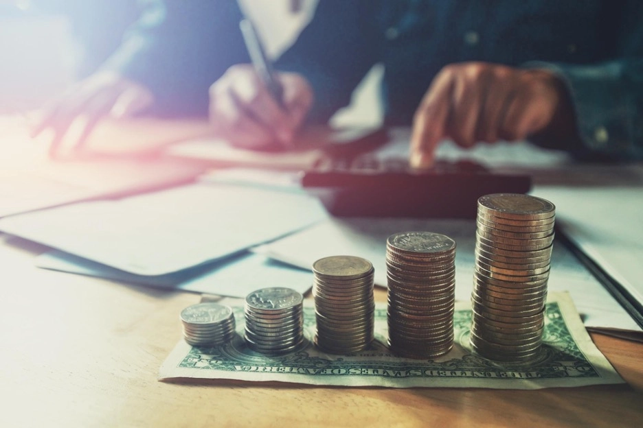 A person calculating cash, with a pile of coins in the front