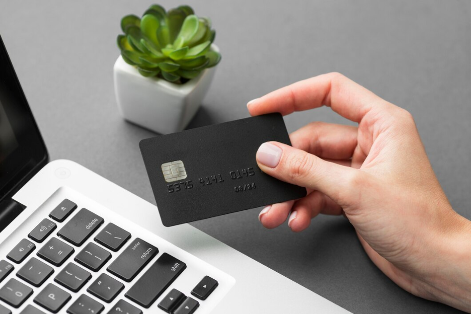 A hand holding a credit card with a laptop in the background