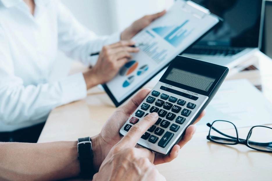 An image indicating two people working with a calculator and charts, and statistics