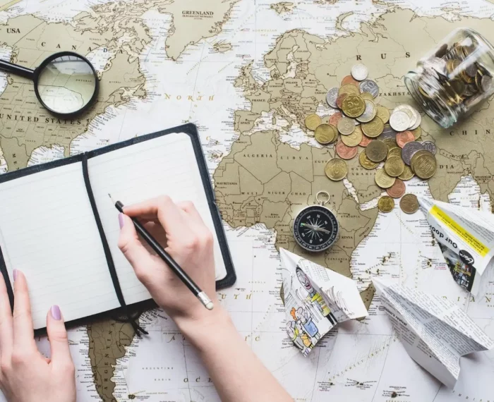 A journal, magnifying glass, compass, coins, and paper planes on top of a world map