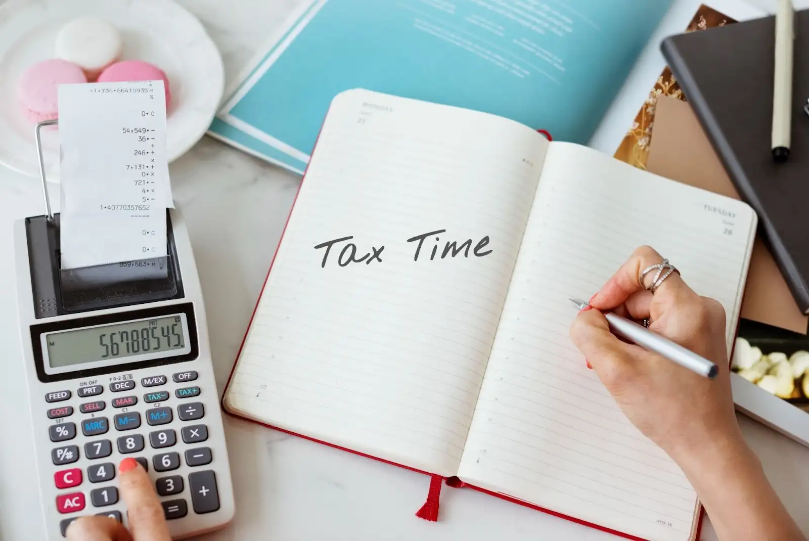 A person using a calculator, a notebook, and a pen to compute tax