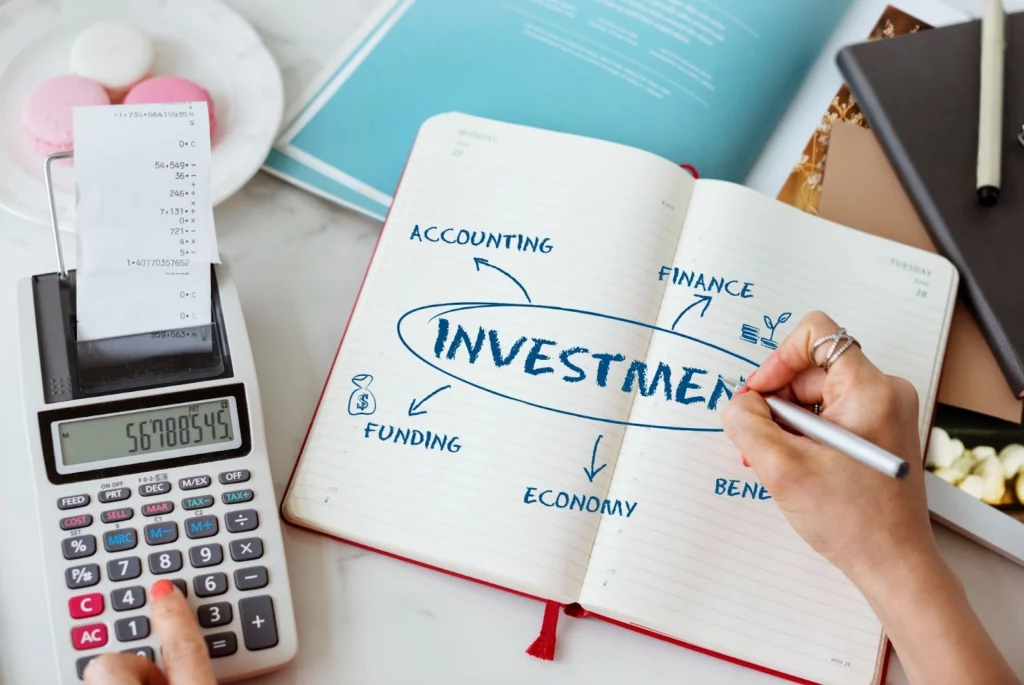 Person using a calculator and writing notes about an investment in a notebook.