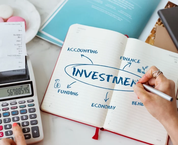 Person using a calculator and writing notes about an investment in a notebook.