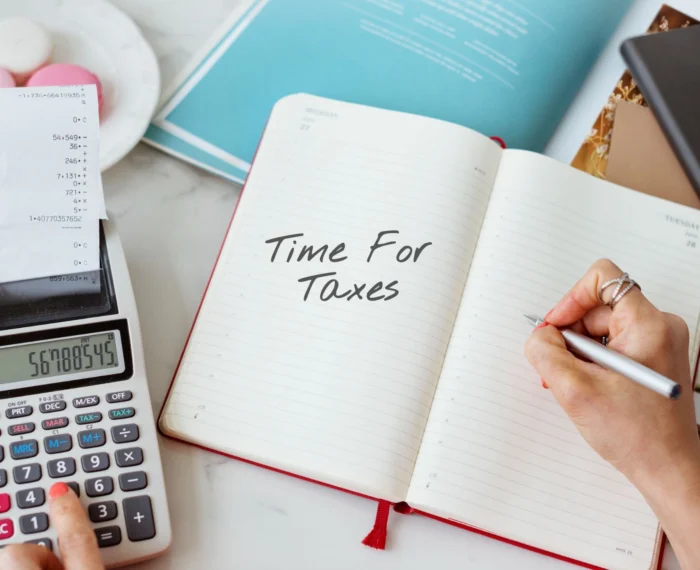 A pencil, calculator, receipt, and notebook with the words “Time For Taxes”