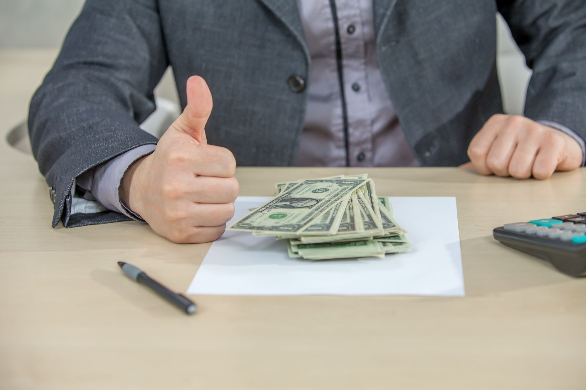 A pile of cash on the table and a man in suit doing thumbs up